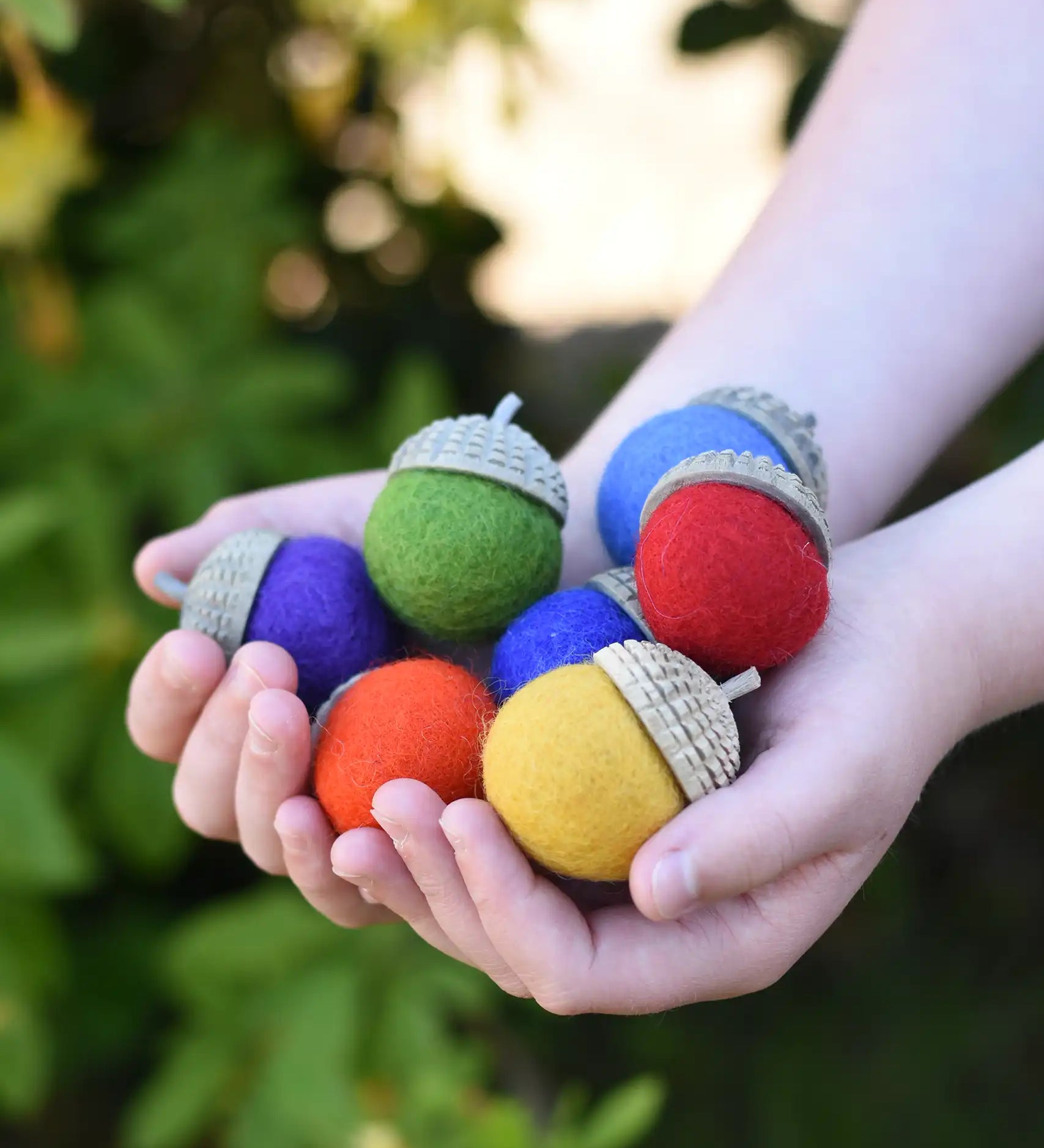 Papoose Toys rainbow acorns in a child's hands. 7 colours of rainbow felt on hand carved wooden acorn caps.