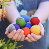 Papoose Toys rainbow acorns in a child's hands. 7 colours of rainbow felt on hand carved wooden acorn caps.