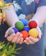 Papoose Toys rainbow acorns in a child's hands. 7 colours of rainbow felt on hand carved wooden acorn caps.