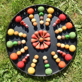 Close up of the Papoose felt balls placed in a mandala with Grapat mandala pieces on a black metal tray. 