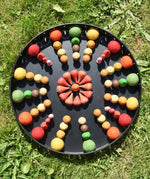 Close up of the Papoose felt balls placed in a mandala with Grapat mandala pieces on a black metal tray. 