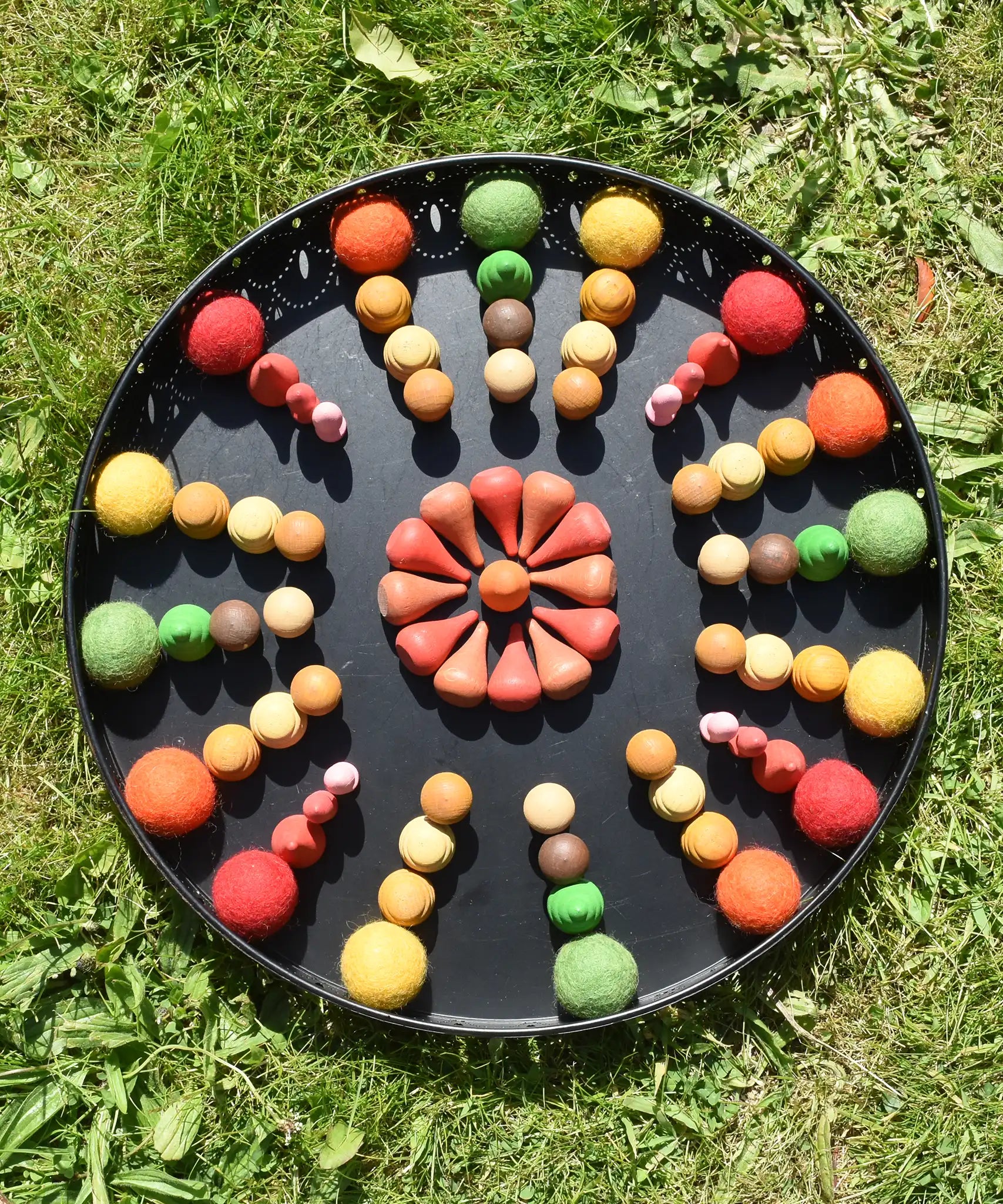 Close up of the Papoose felt balls placed in a mandala with Grapat mandala pieces on a black metal tray. 