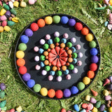 Papoose rainbow felt balls placed in a mandala with Grapat mandala pieces on a black metal tray. 