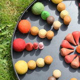 Close up of the Papoose felt balls placed in a mandala with Grapat mandala pieces on a black tray. 
