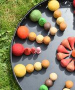 Close up of the Papoose felt balls placed in a mandala with Grapat mandala pieces on a black tray. 