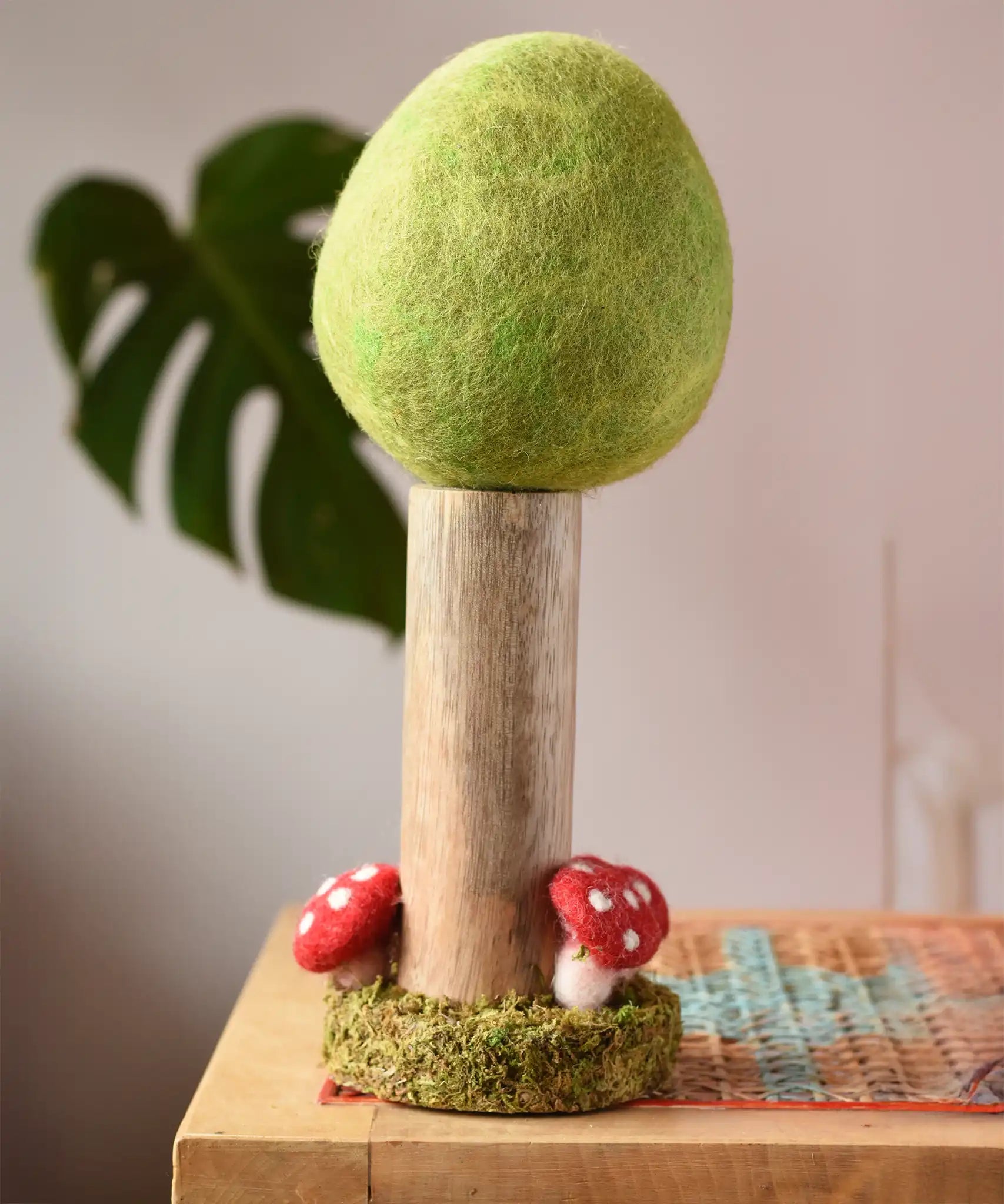 Papoose Toys Spring felt woodland tree placed on a rattan top stool. 