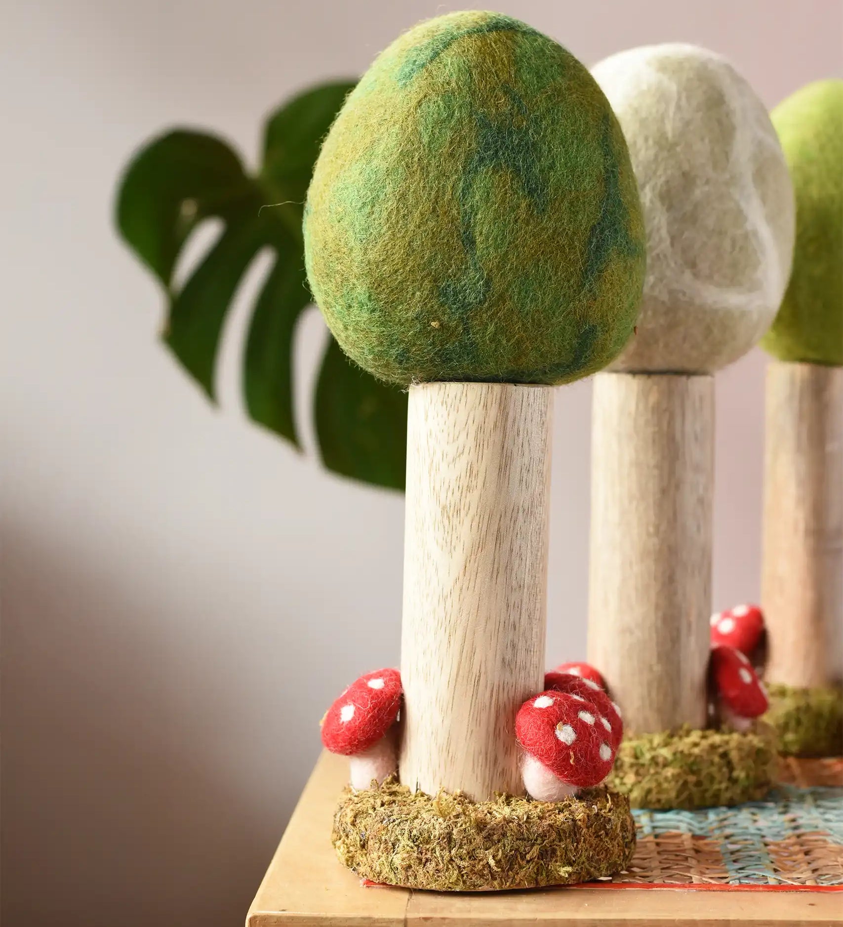 Papoose Toys Summer felt woodland tree placed on a rattan top stool. Winter and Spring versions can be seen in the background. 