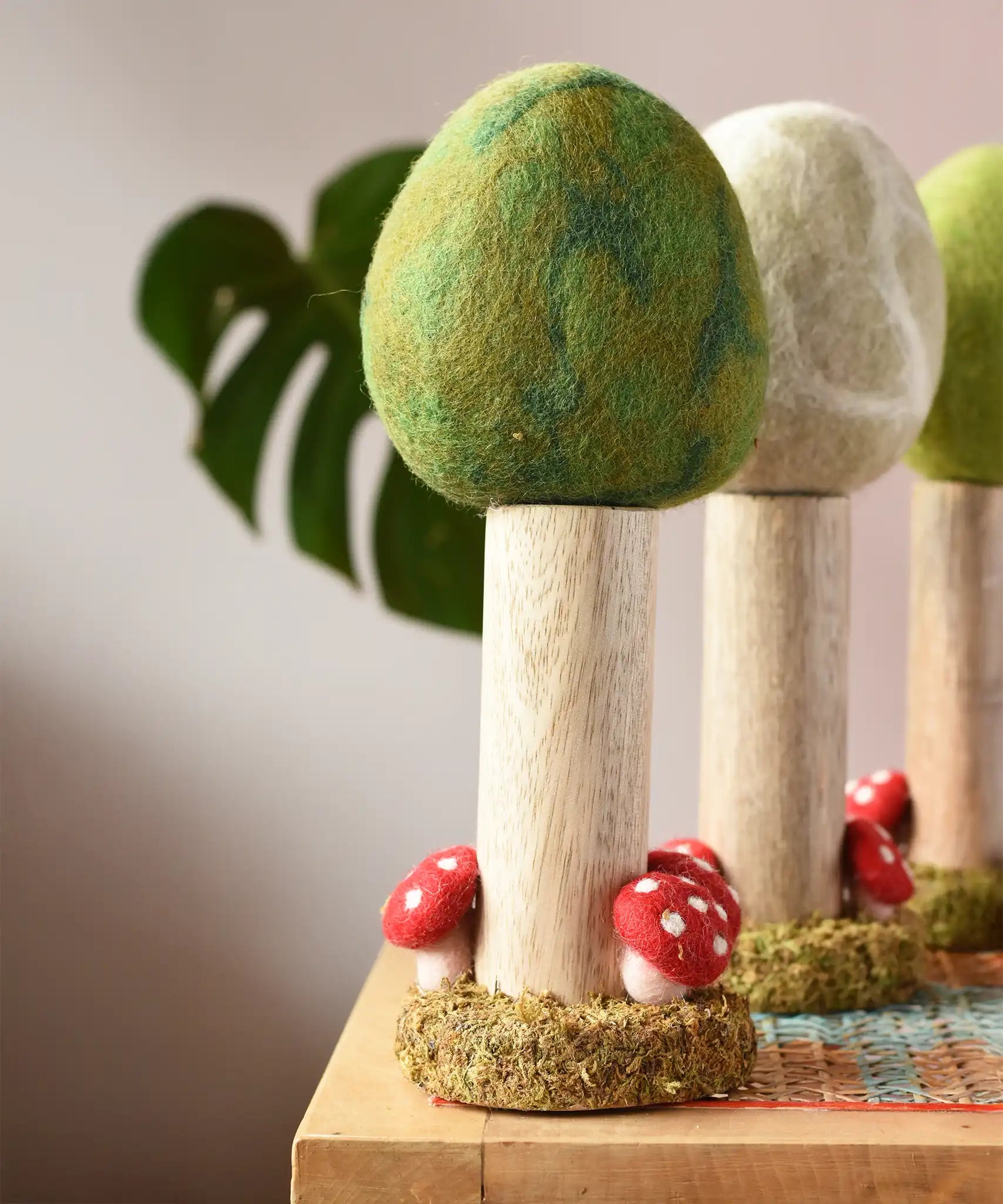 Papoose Toys Summer felt woodland tree placed on a rattan top stool. Winter and Spring versions can be seen in the background. 