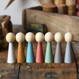 Papoose Toys wooden earth people  peg dolls set of 7 placed on a wooden desk.