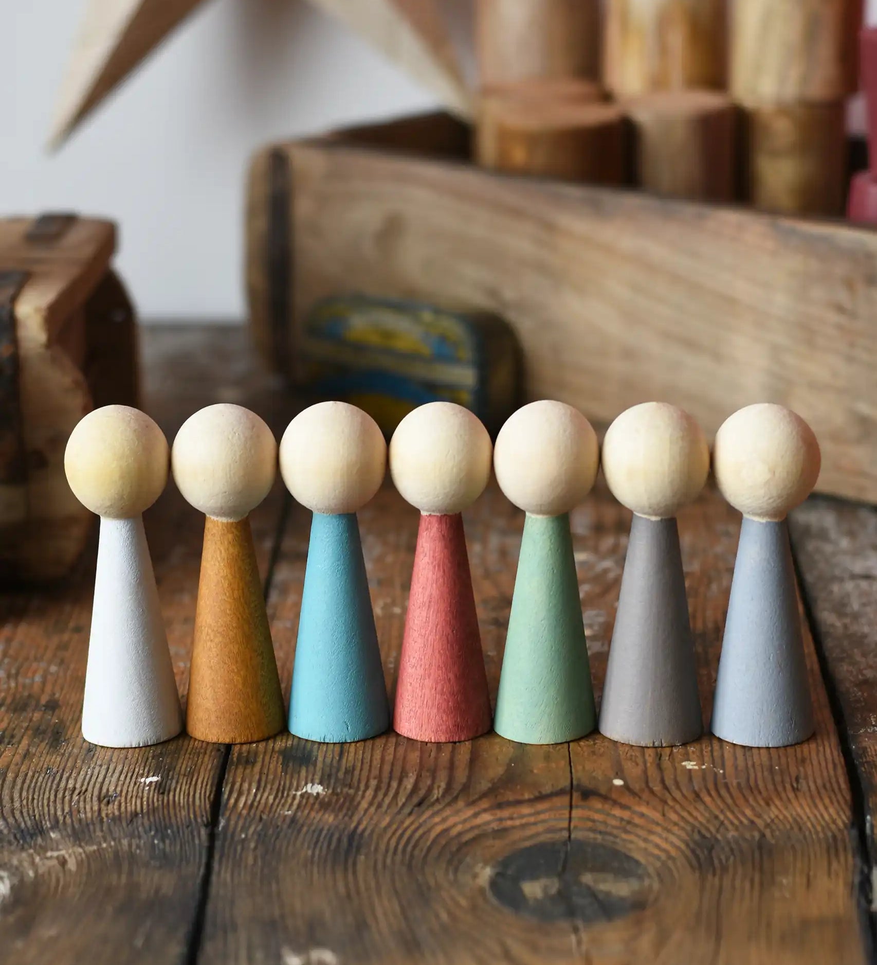 Papoose Toys wooden earth people  peg dolls set of 7 placed on a wooden desk.