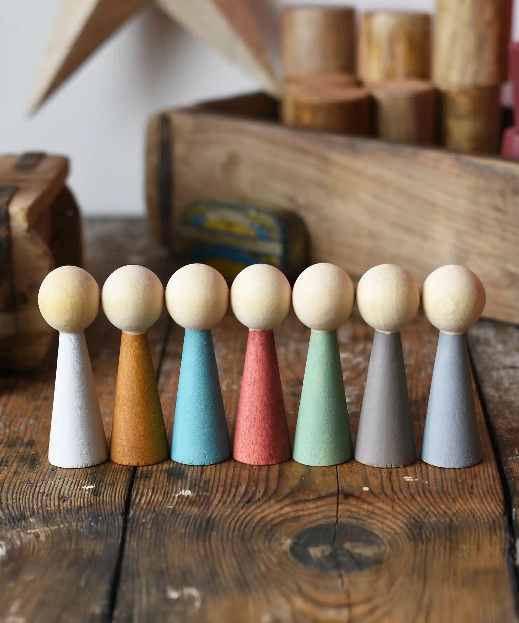 Papoose Toys wooden earth people  peg dolls set of 7 placed on a wooden desk.