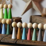 Papoose Toys wooden earth people  peg dolls set of 7 placed on a wooden desk. Goethe rainbow dolls can be seen in the background.