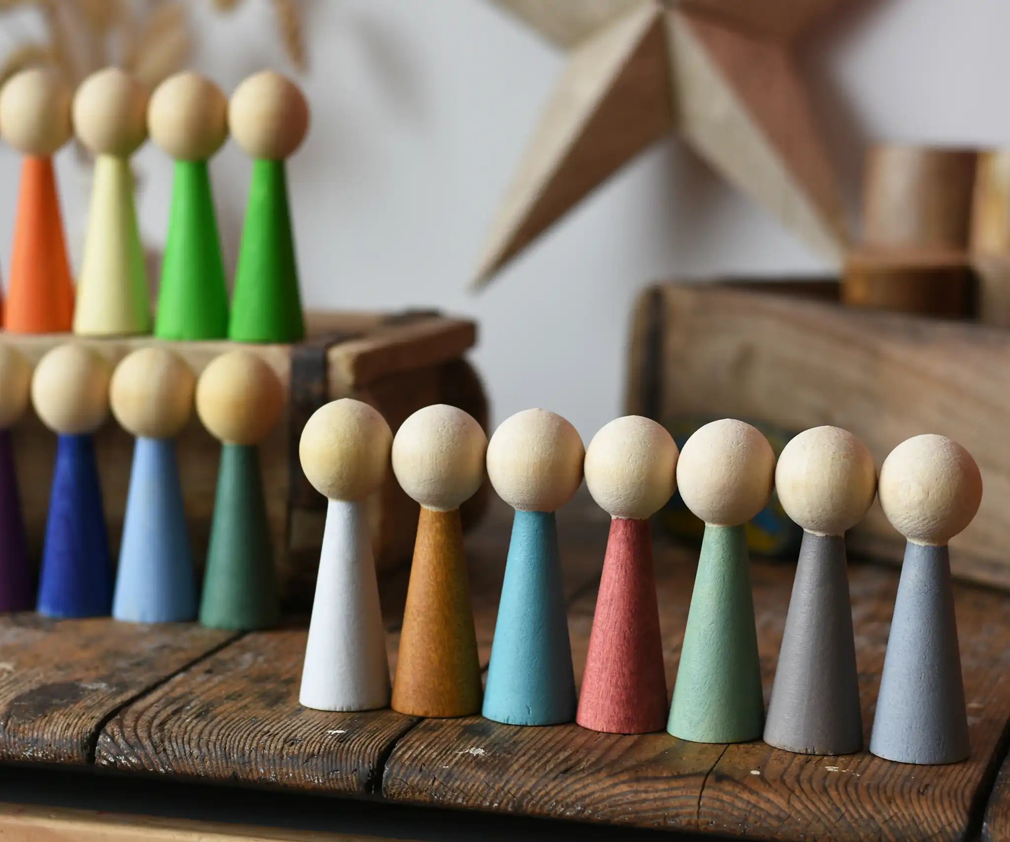 Papoose Toys wooden earth people  peg dolls set of 7 placed on a wooden desk. Goethe rainbow dolls can be seen in the background.