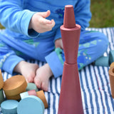 Papoose Toys wooden stacking cones in earth red stacked up by a young child.