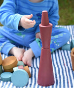 Papoose Toys wooden stacking cones in earth red stacked up by a young child.