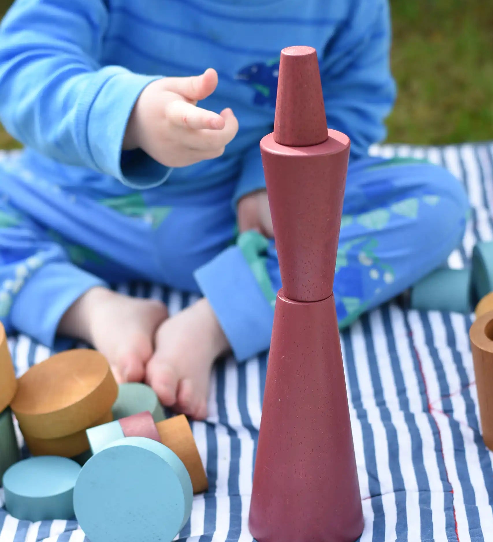 Papoose Toys wooden stacking cones in earth red stacked up by a young child.