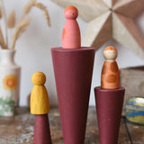 Papoose Toys wooden stacking cones in earth red placed on a wooden desk with Grapat Wild Crew peg dolls placed on them.