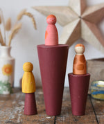 Papoose Toys wooden stacking cones in earth red placed on a wooden desk with Grapat Wild Crew peg dolls placed on them.