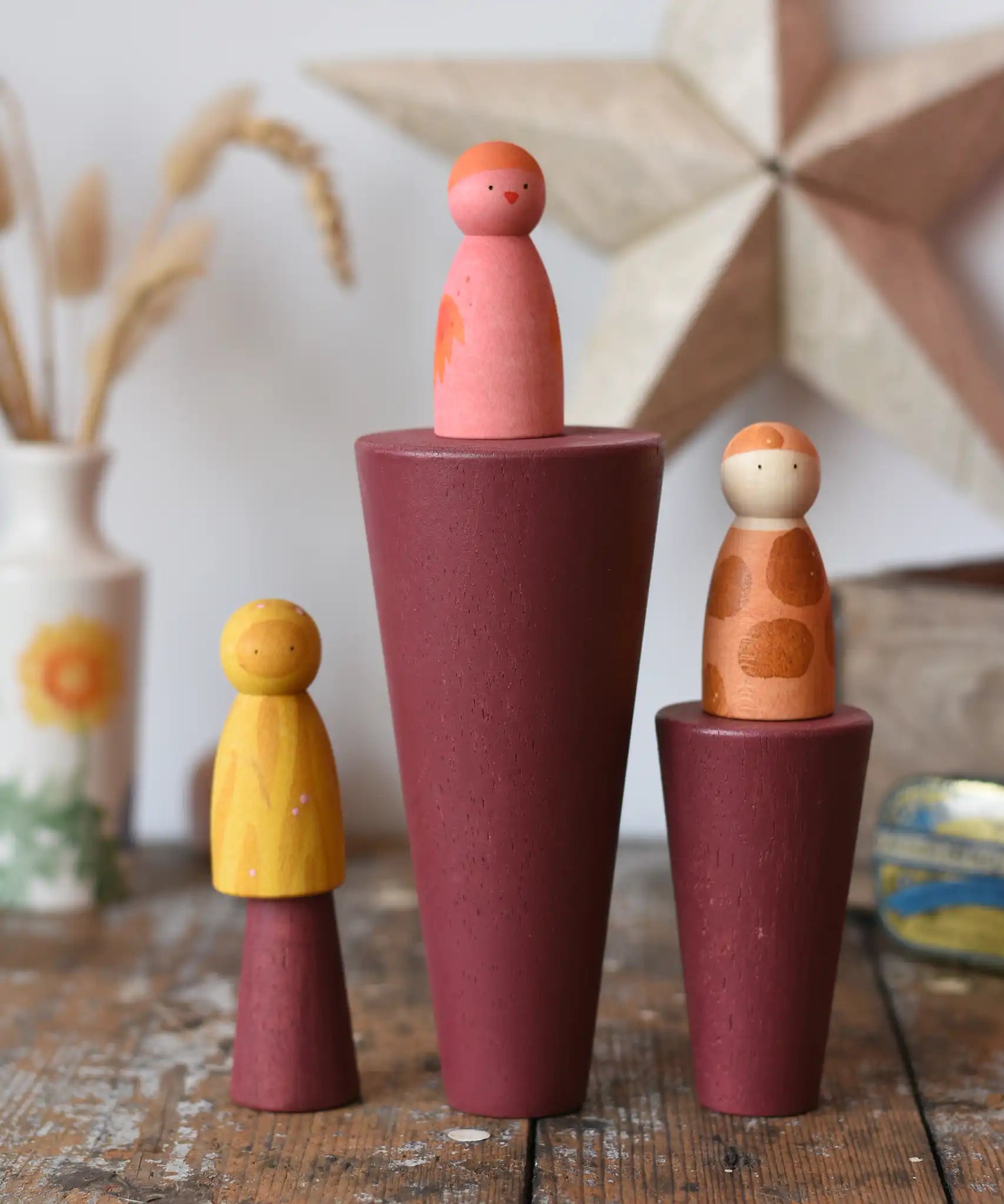 Papoose Toys wooden stacking cones in earth red placed on a wooden desk with Grapat Wild Crew peg dolls placed on them.