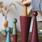 Papoose Toys wooden stacking cones in earth red with peg dolls being placed on them.