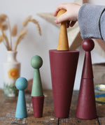 Papoose Toys wooden stacking cones in earth red with peg dolls being placed on them.