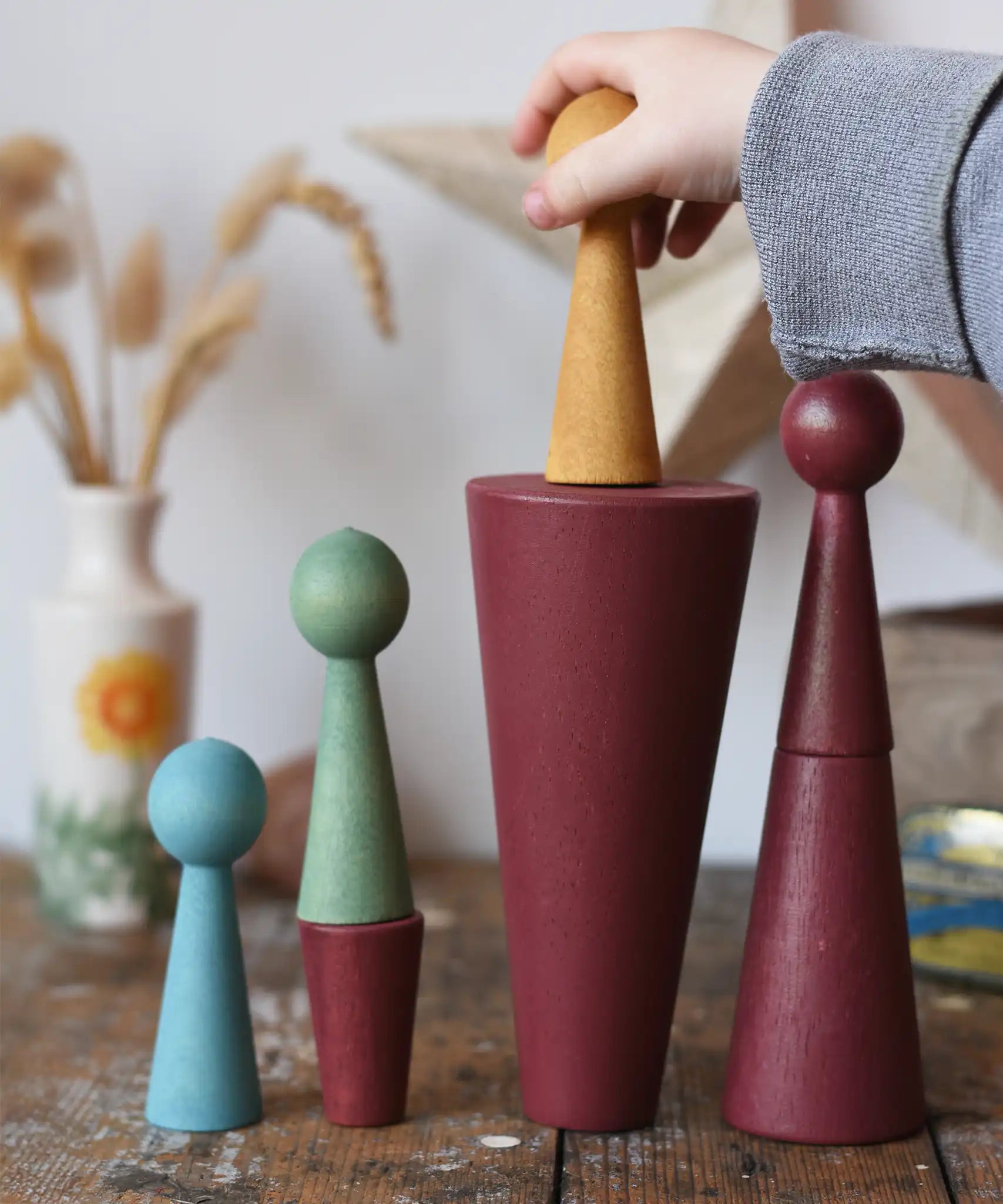 Papoose Toys wooden stacking cones in earth red with peg dolls being placed on them.