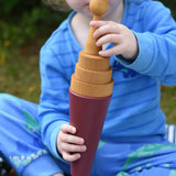 Child using a Papoose Toys wooden stacking cone in earth red as an ice cream cone with yellow discs and a yellow peg doll on top.