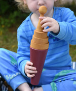 Child using a Papoose Toys wooden stacking cone in earth red as an ice cream cone with yellow discs and a yellow peg doll on top.