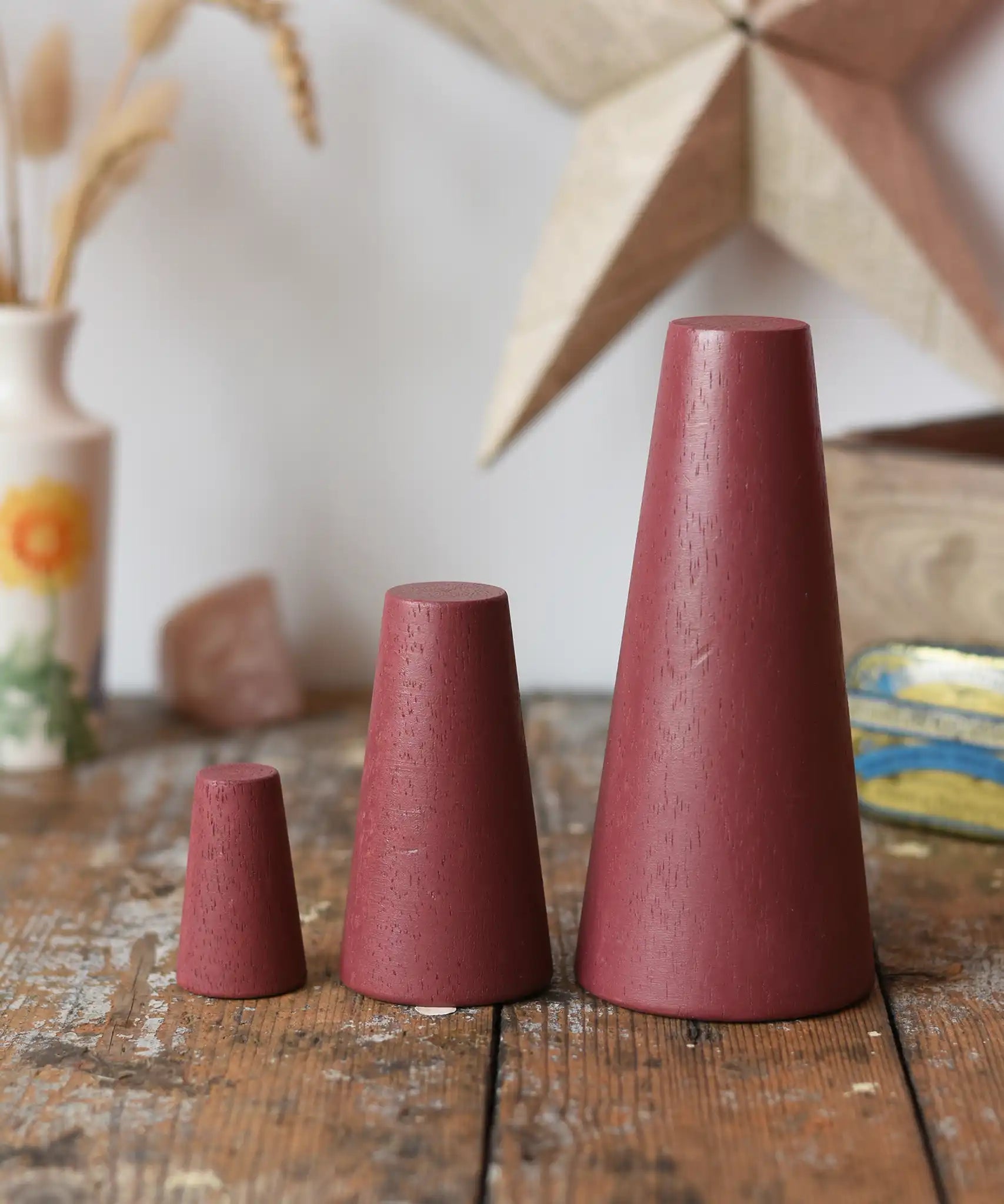 Papoose Toys wooden stacking cones in earth red placed on a wooden desk.

