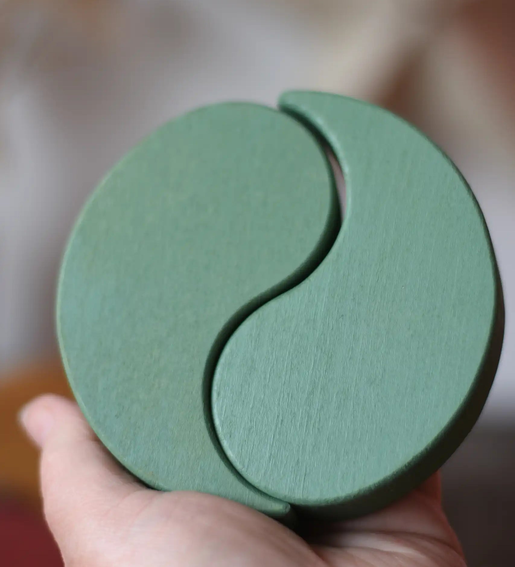 Papoose Toys wooden earth yim yams in green in an adult's hand. 