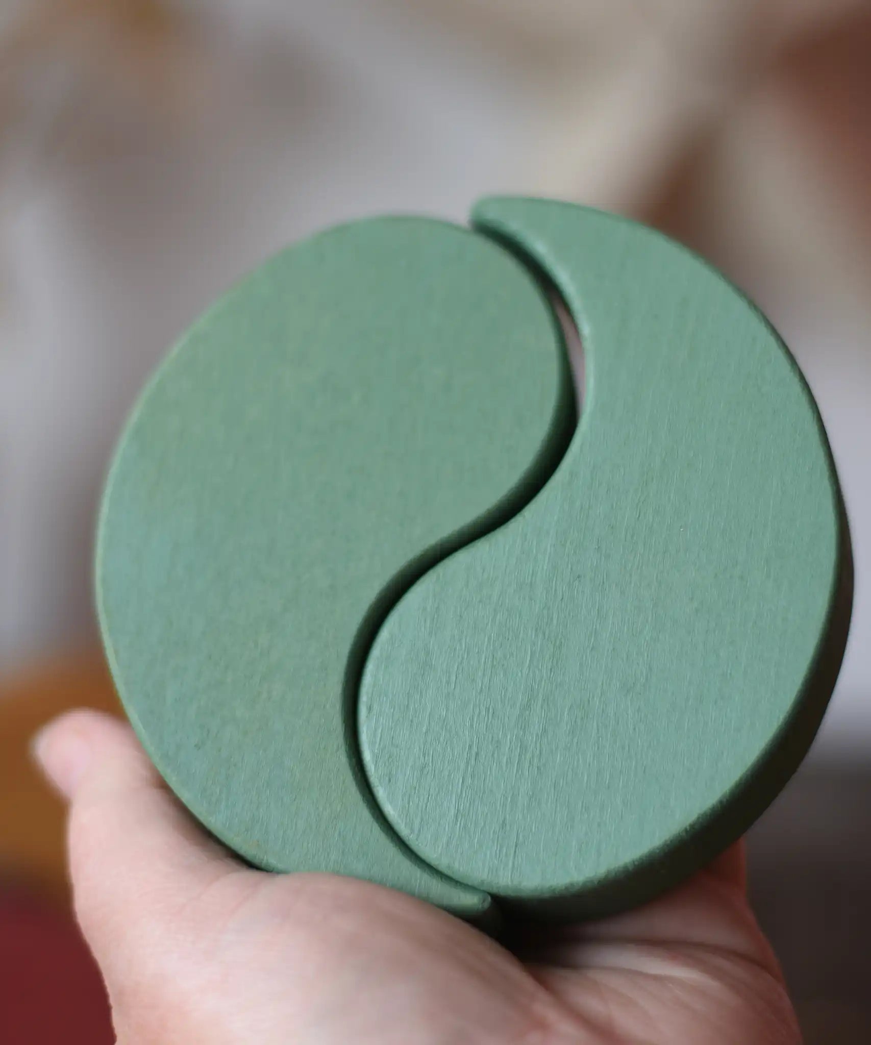 Papoose Toys wooden earth yim yams in green in an adult's hand. 