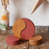 Papoose Toys wooden earth yim yam in red and yellow placed on a wooden desk.