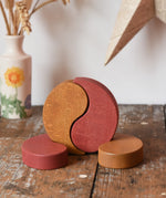 Papoose Toys wooden earth yim yam in red and yellow placed on a wooden desk.