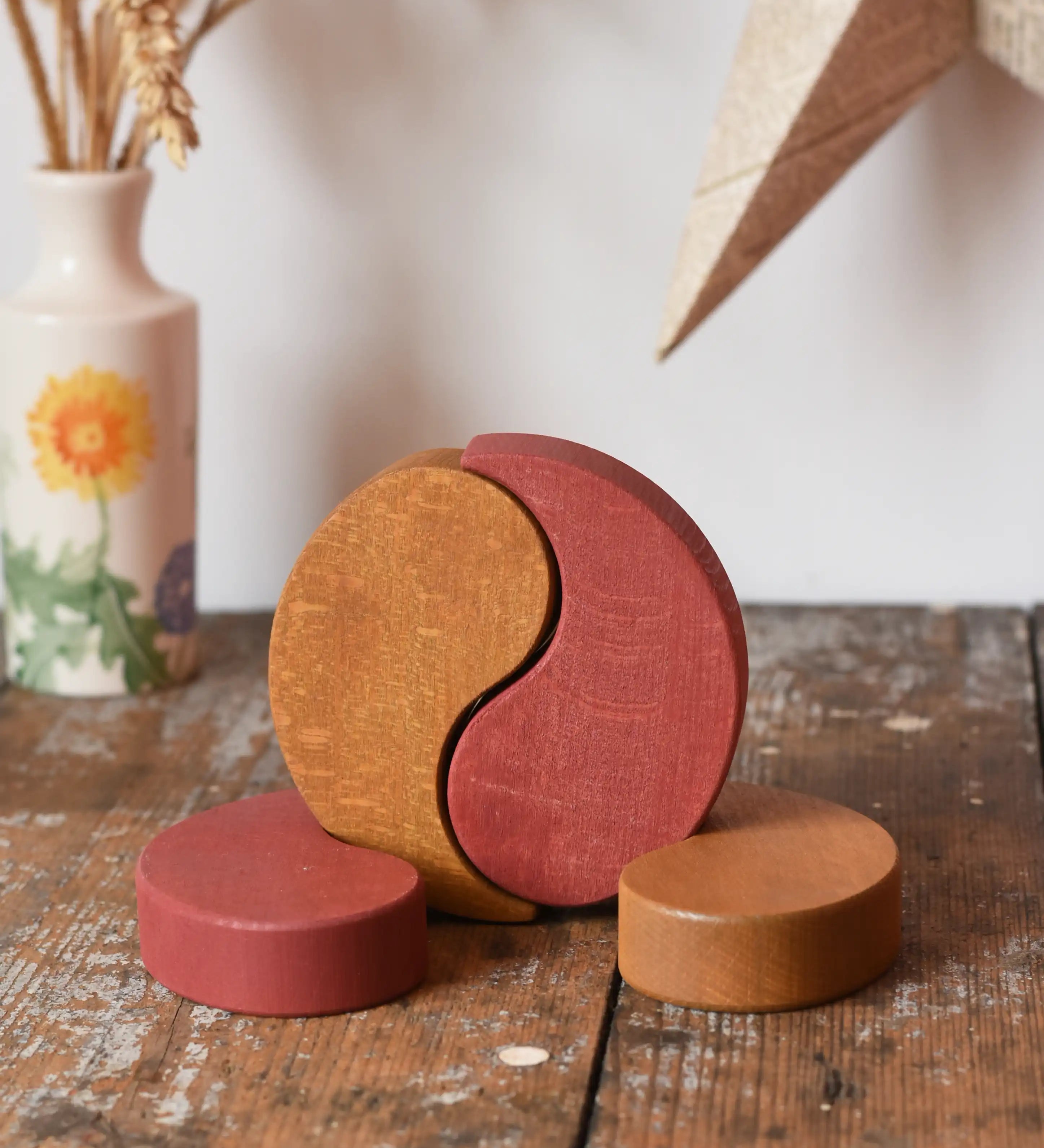 Papoose Toys wooden earth yim yam in red and yellow placed on a wooden desk.