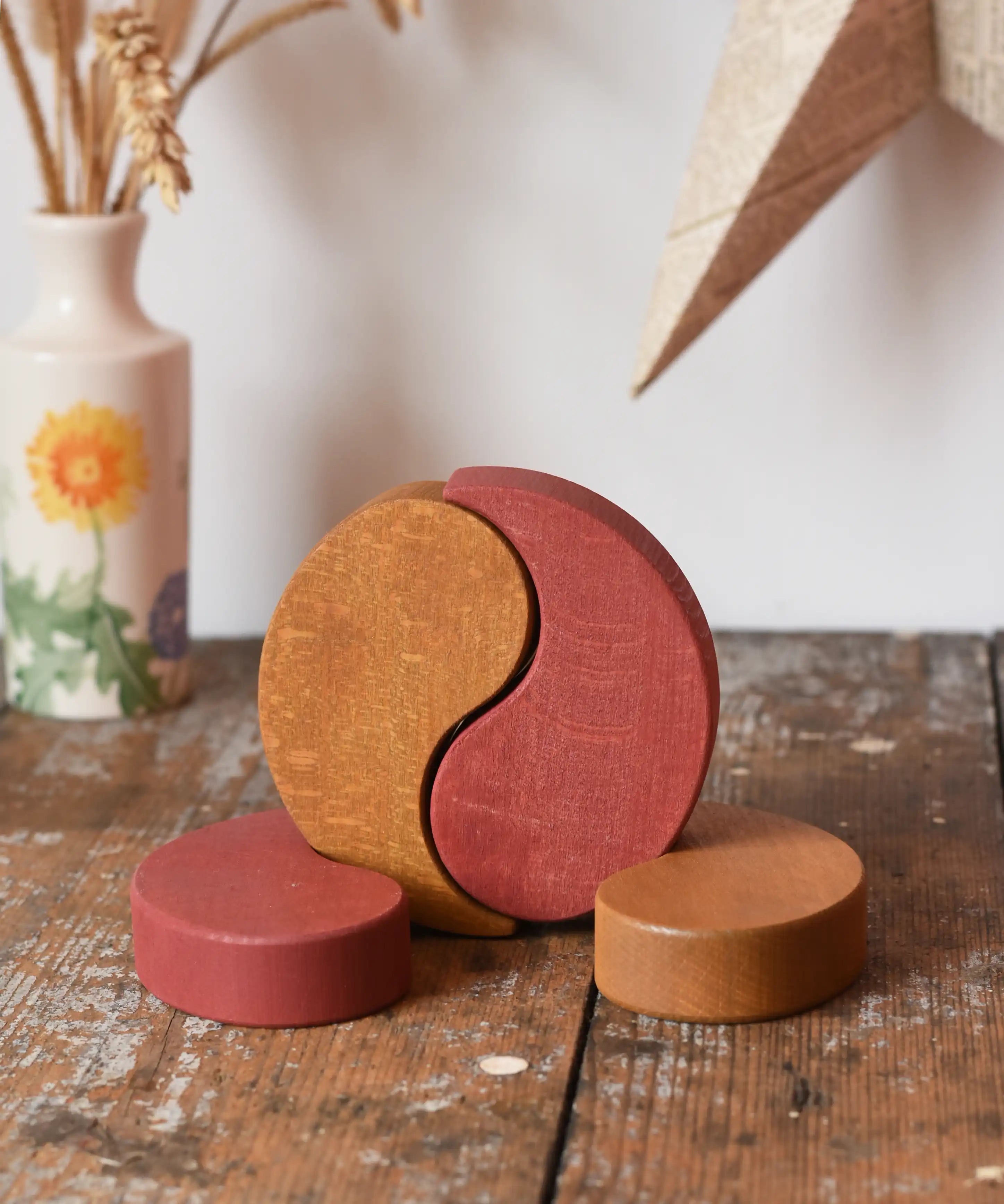 Papoose Toys wooden earth yim yam in red and yellow placed on a wooden desk.