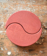 Papoose Toys wooden earth yim yam in red placed on a wooden desk.