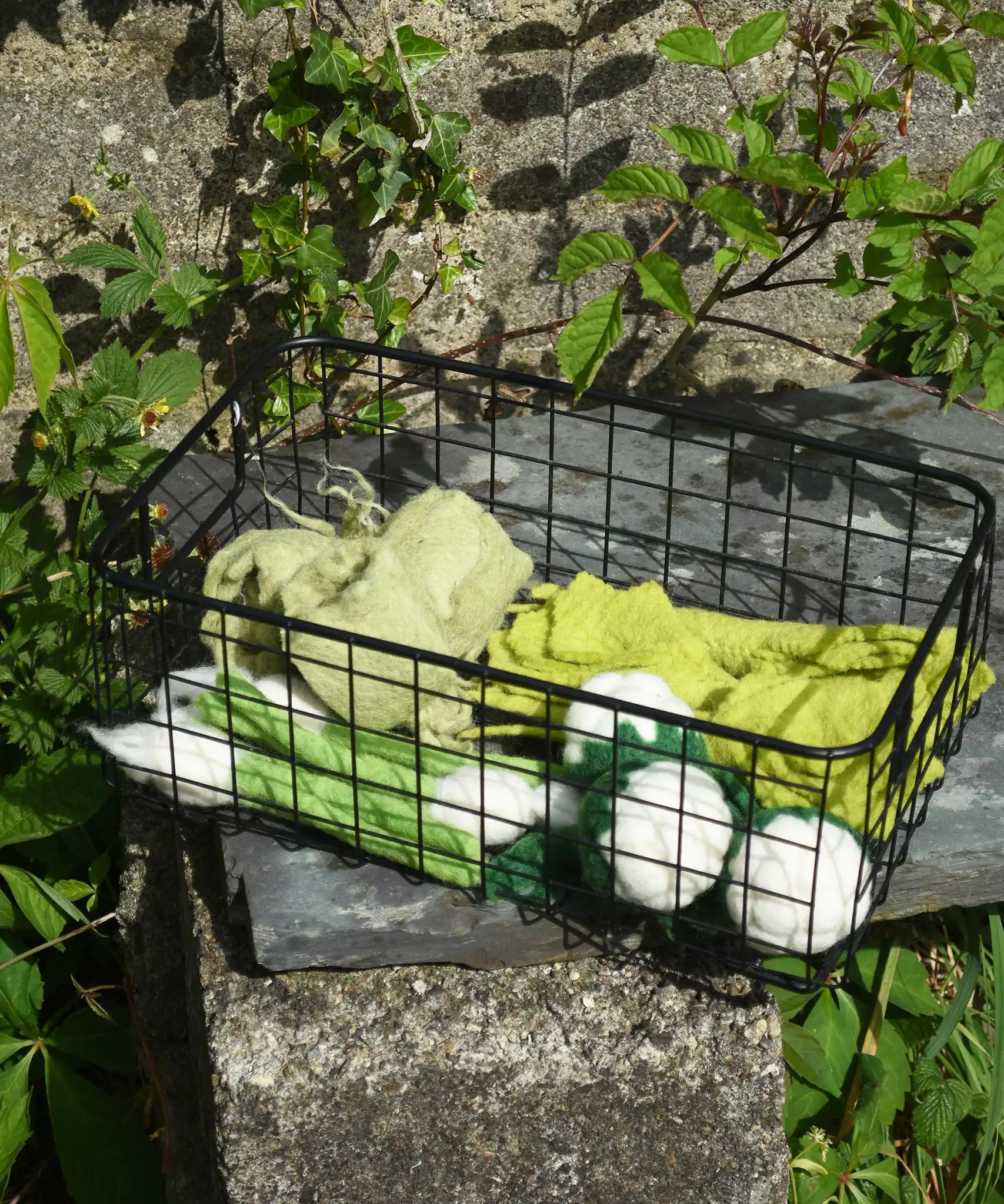 Papoose Toys felt vegetable play food placed in a black wire basket.