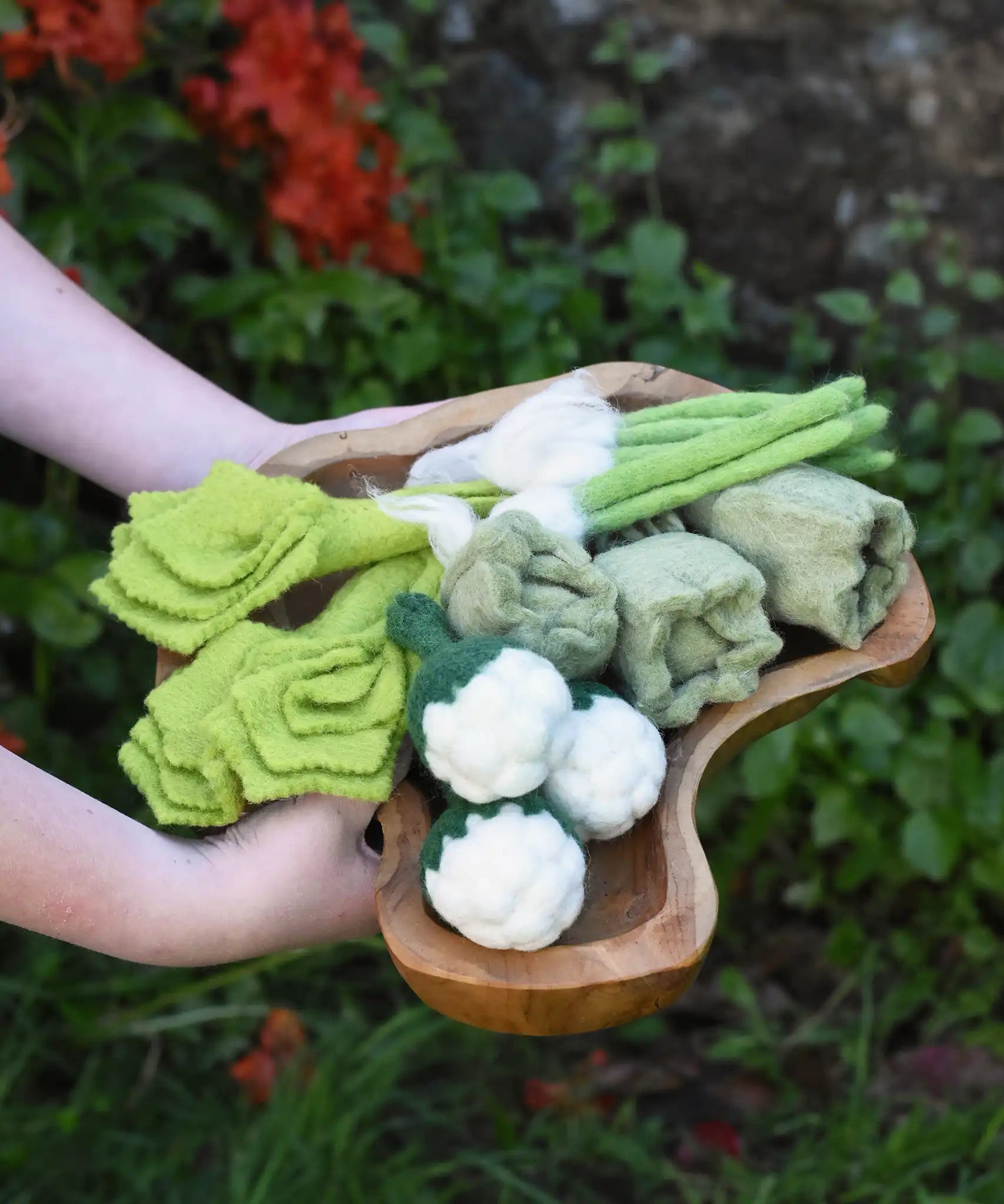 Papoose Toys felt vegetable play food in a wooden dish, held by a child.