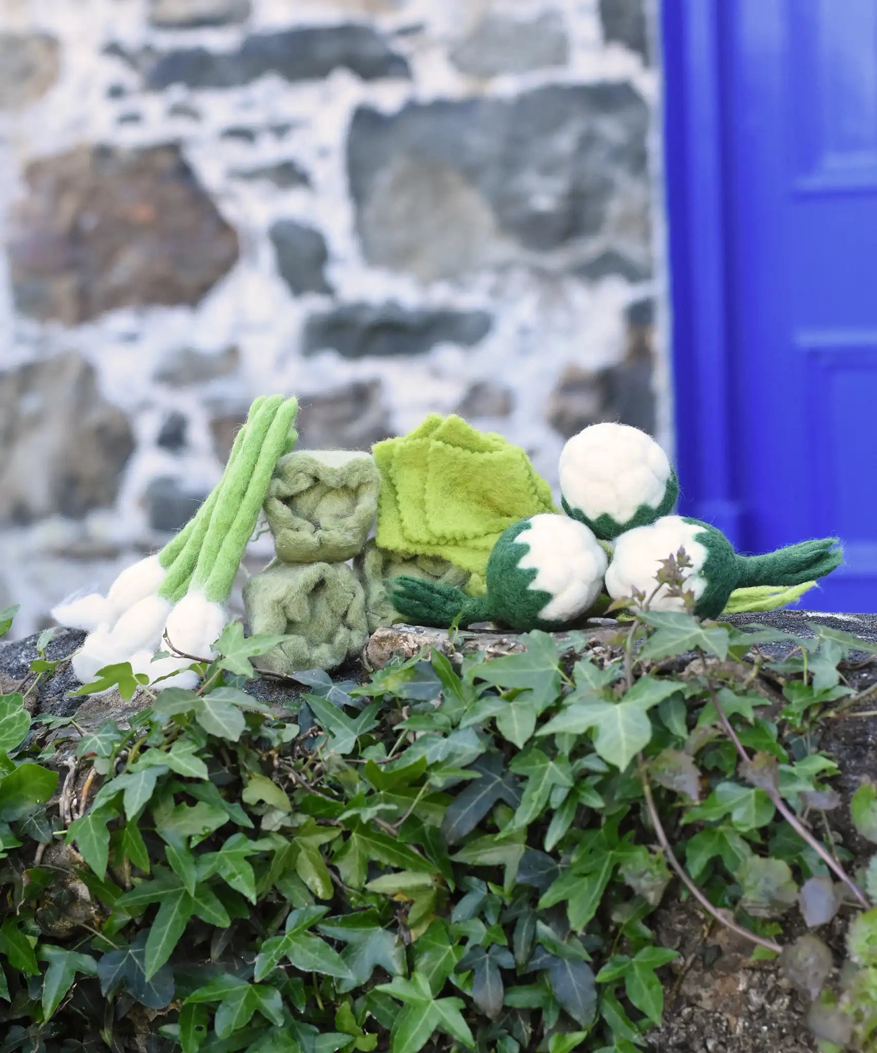 Papoose Toys felt vegetable play food placed on a stone wall outdoors.