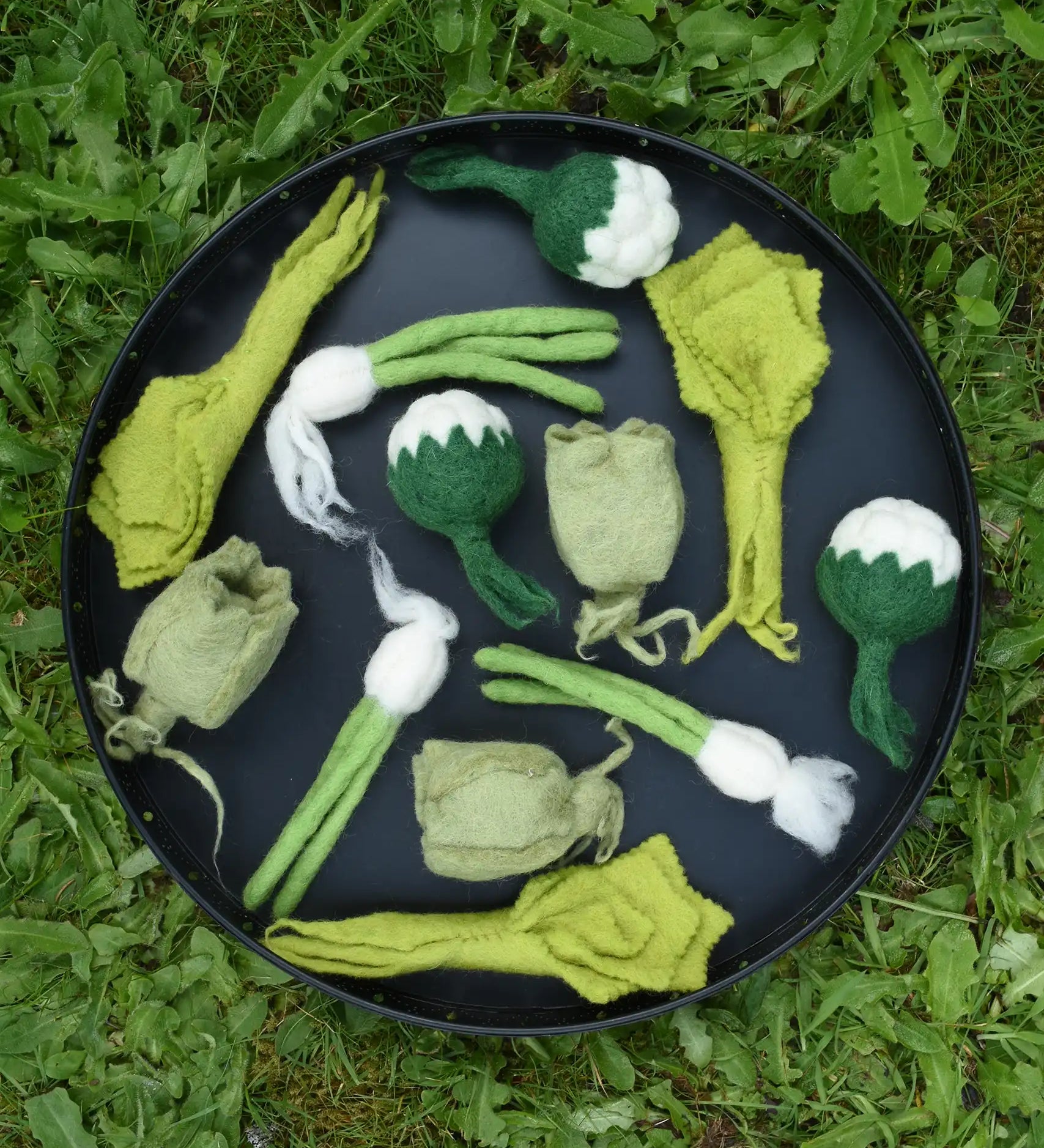 Papoose Toys felt vegetable play food placed on a black tray outdoors.  