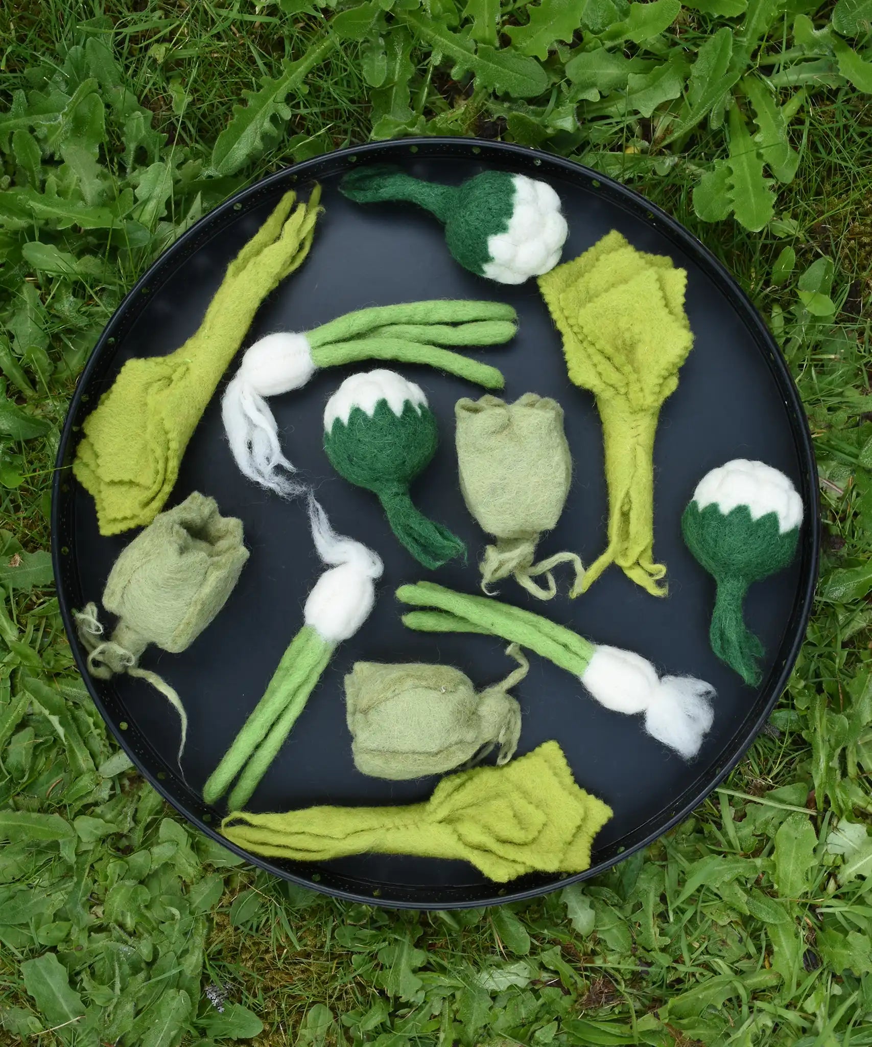 Papoose Toys felt vegetable play food placed on a black tray outdoors.  
