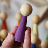 Purple Papoose Toys wooden Goethe rainbow people peg doll in an adult's hand.