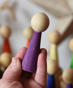 Purple Papoose Toys wooden Goethe rainbow people peg doll in an adult's hand.