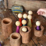 Papoose Toys 12 wooden Goethe rainbow people peg dolls placed on a wooden desk with some placed into wooden stacking tubes.