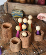 Papoose Toys 12 wooden Goethe rainbow people peg dolls placed on a wooden desk with some placed into wooden stacking tubes.