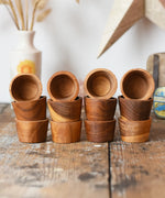 Papoose Toys 12 small natural wooden bowls placed on a wooden desk. 