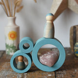Papoose Toys nesting tubes in earth blue stacked on a wooden desk with Grapat Nins placed on them. 