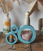 Papoose Toys nesting tubes in earth blue stacked on a wooden desk with Grapat Nins placed on them. 