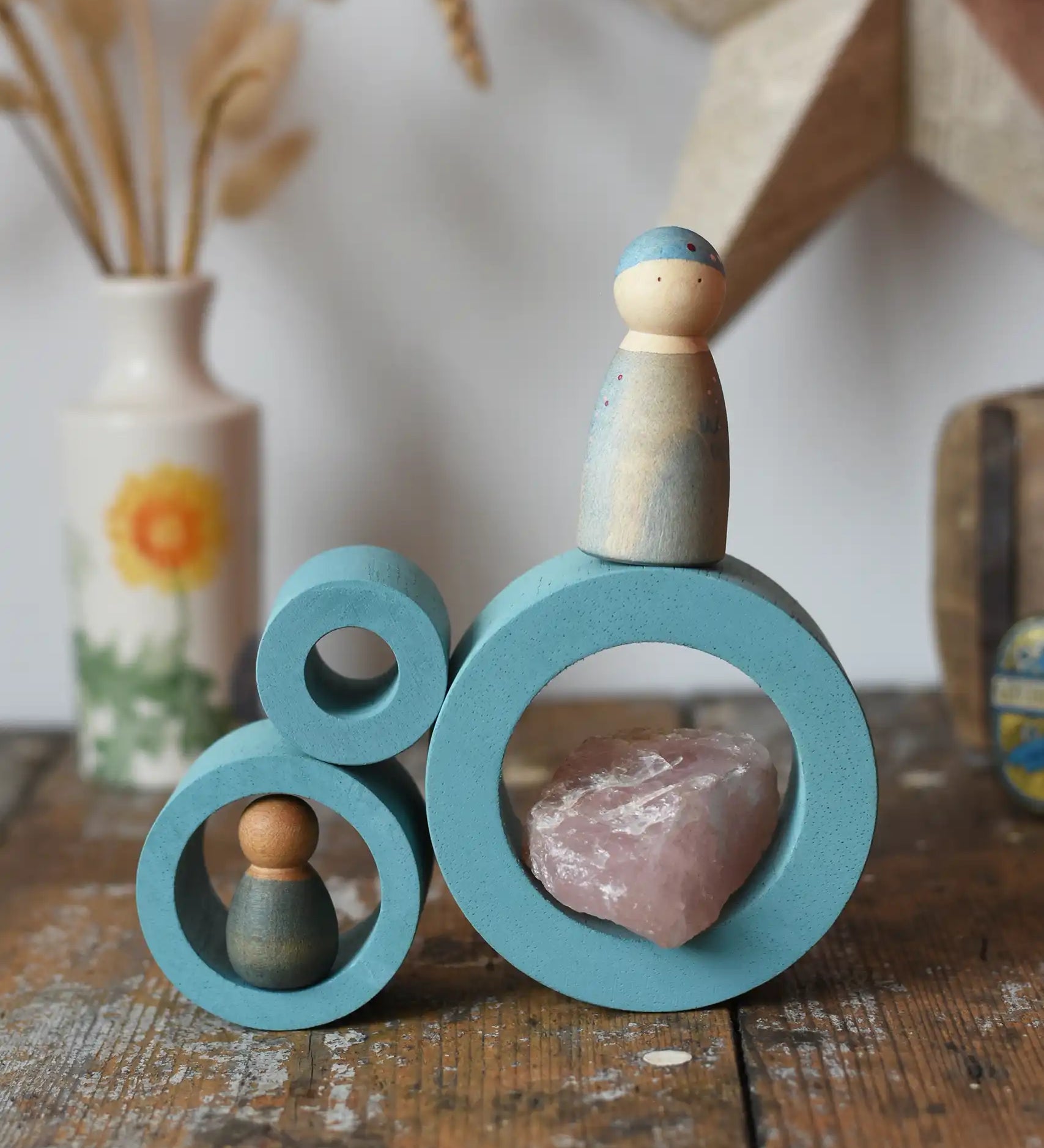 Papoose Toys nesting tubes in earth blue stacked on a wooden desk with Grapat Nins placed on them. 