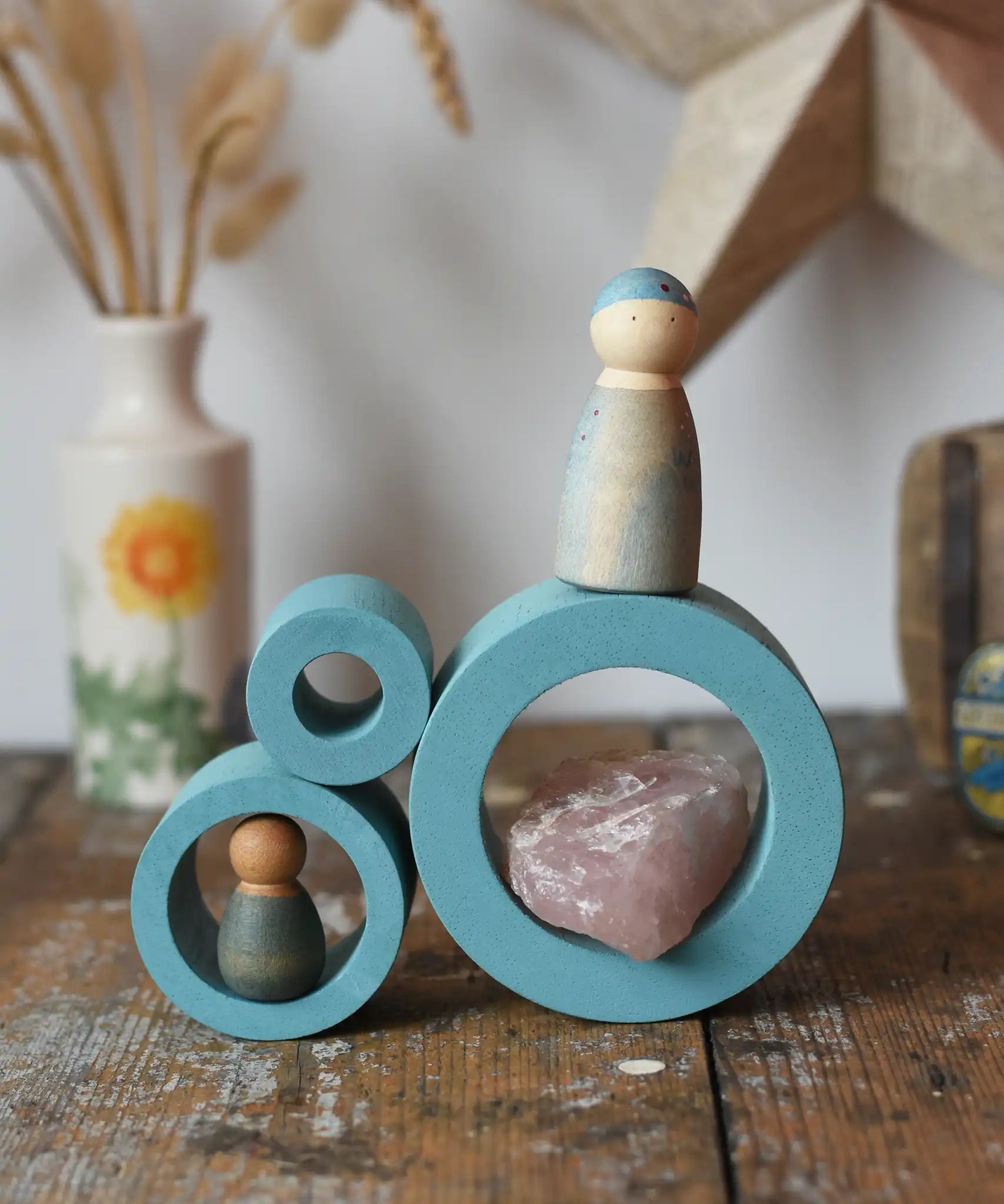 Papoose Toys nesting tubes in earth blue stacked on a wooden desk with Grapat Nins placed on them. 